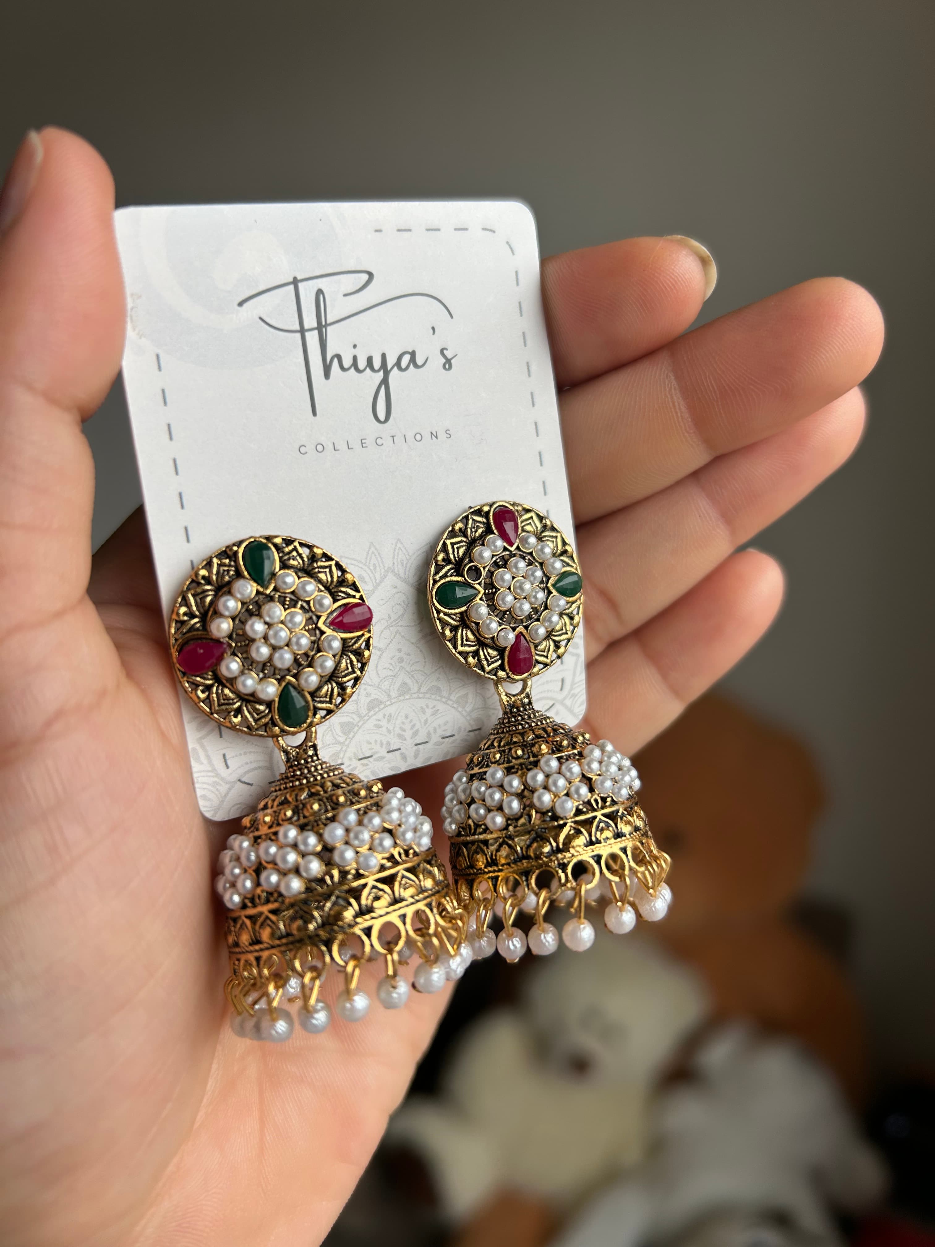 Thiya's Tricolor Pearl Jhumka mit dunklem Gold Finish und geometrischen Gravuren weiße Perlen und grüne rote Tränensteine